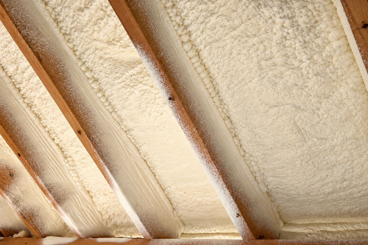 Open-cell spray foam fills the spaces between exposed wooden roof rafters.